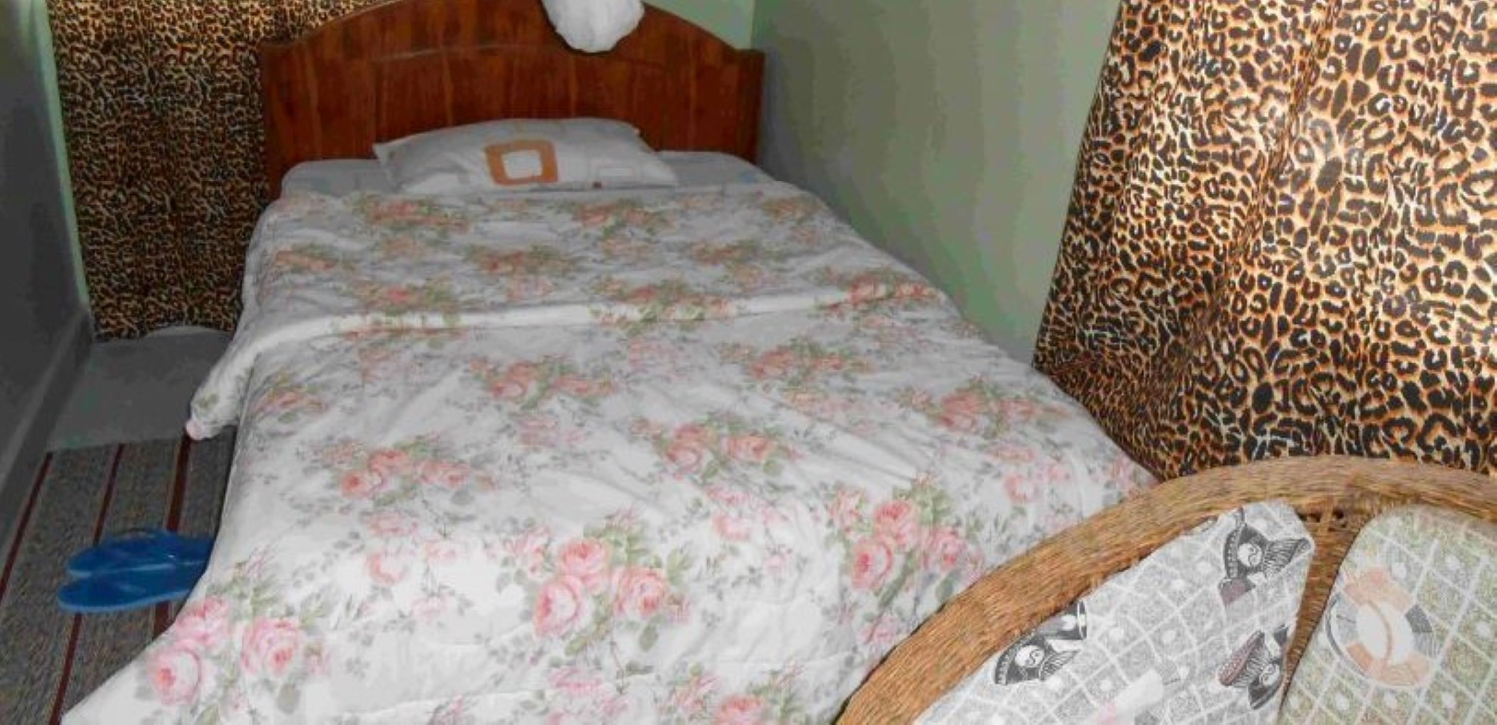 A single bed with a floral bedspread, a wooden headboard, and a leopard print chair.