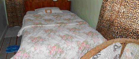 A single bed with a floral bedspread, a wooden headboard, and a leopard print chair.