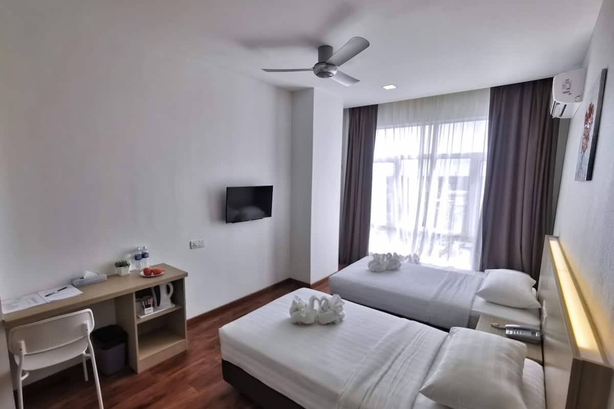A hotel room with two beds, a desk, a chair, a TV, and a ceiling fan.