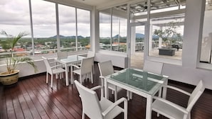A spacious balcony with a glass table and white wicker chairs, overlooking a cityscape with mountains in the distance. - Green World Hotel (Semporna)