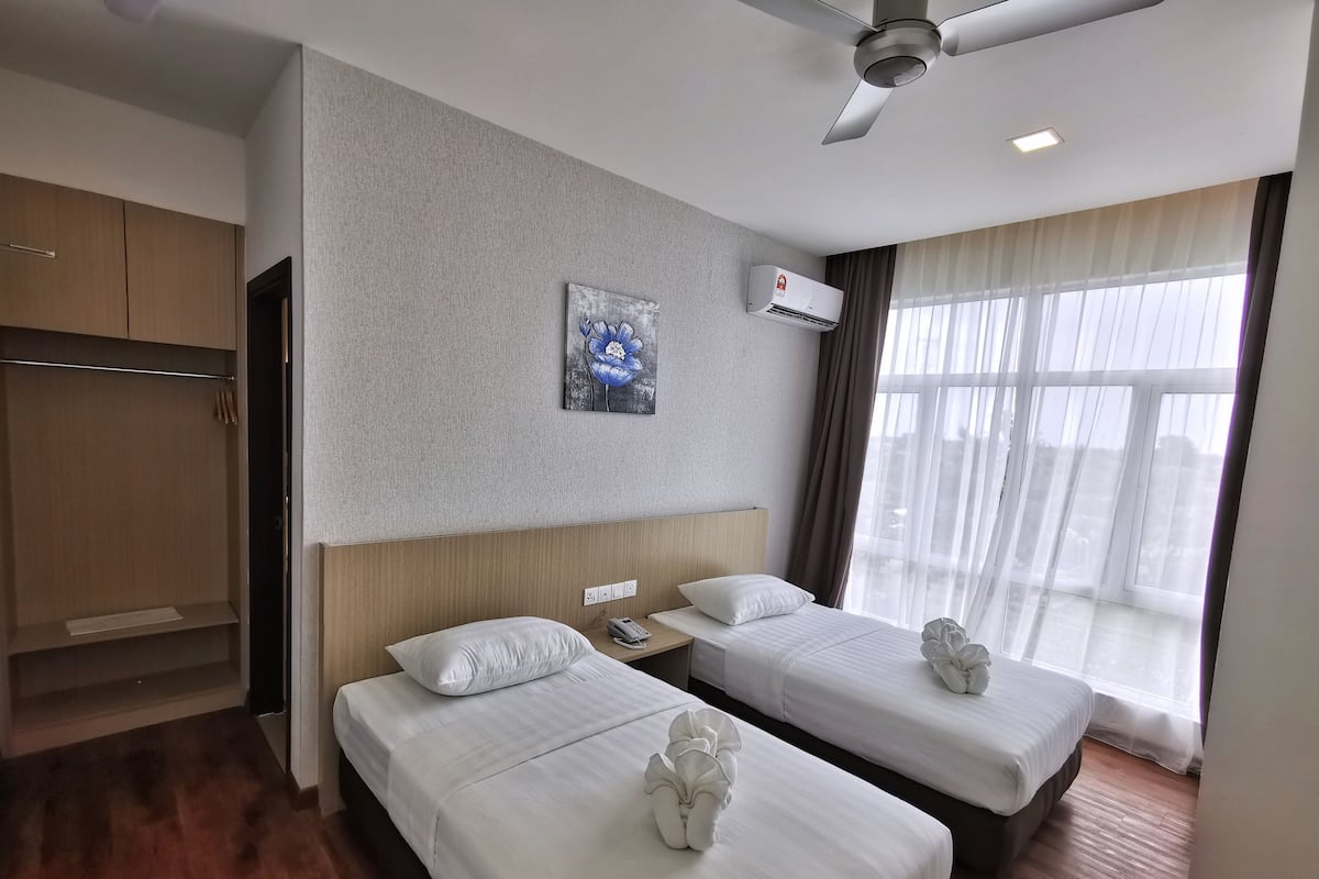 A hotel room with two beds, a ceiling fan, an air conditioning unit, a painting, and a view of the outdoors through large windows.