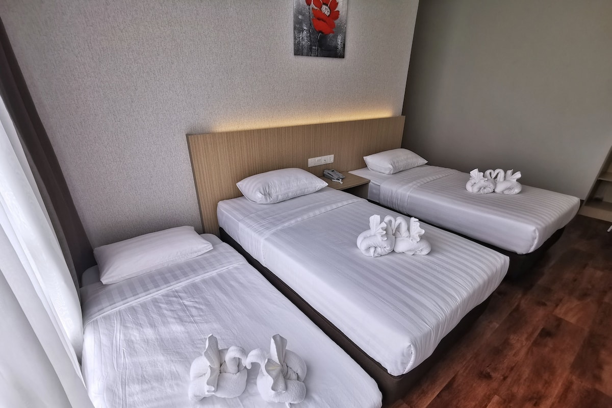 A hotel room with three single beds, each with white linens and decorative swan-shaped towels.