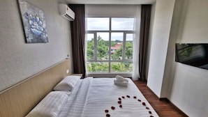 A hotel room with a bed, a painting on the wall, an air conditioning unit, a window with curtains, and a television mounted on the wall. - Green World Hotel (Semporna)
