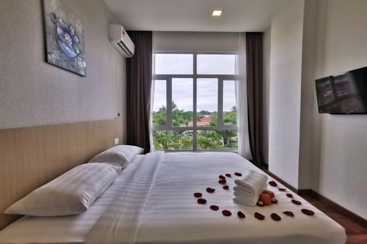 Habitación de hotel con un ventanal grande, cama con ropa de cama blanca y televisor de pantalla plana en la pared.