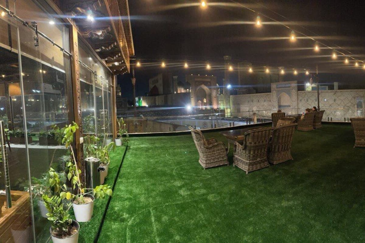 An outdoor seating area with wicker chairs and a hanging chair, surrounded by potted plants and string lights.
