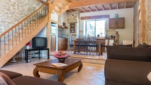 Un intérieur rustique avec un mur en pierre, un escalier en bois, un coin repas avec une table et des chaises, et un salon avec des canapés.