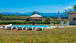 Un espace piscine avec des chaises longues, un belvédère et une vue sur les montagnes lointaines.
