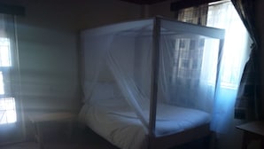 Una cama individual con dosel en una habitación con suelo de baldosas y un ventanal con cortinas.