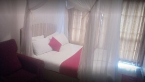 Quarto de hotel com cama, cadeira e cortinas leves.