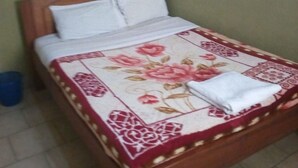 A bed with a floral bedspread, a wooden headboard, and a blue mosquito net. - Liwa Guest House (Naivasha)