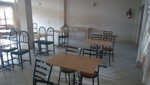 A spacious room with multiple tables and chairs, a fire extinguisher on the wall, and a window providing natural light. - Liwa Guest House (Naivasha)