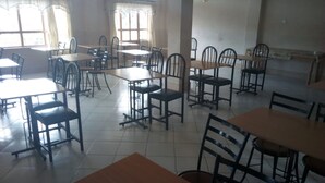 A spacious dining area with multiple tables and chairs, large windows allowing natural light, and a tiled floor. - Liwa Guest House (Naivasha)