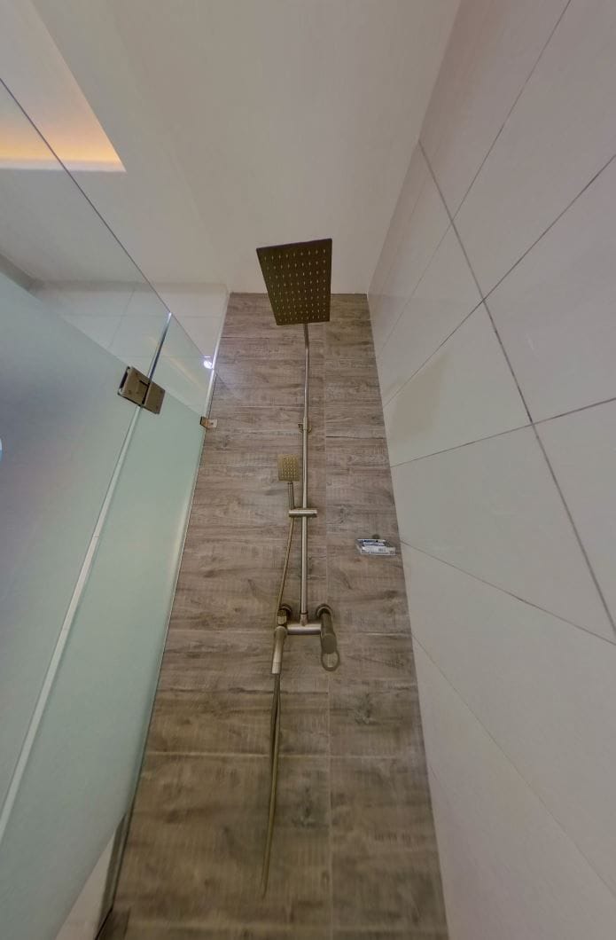 Ein modernes Badezimmer mit Glasabtrennung, Holzboden und Dusche mit eckigem Duschkopf.
