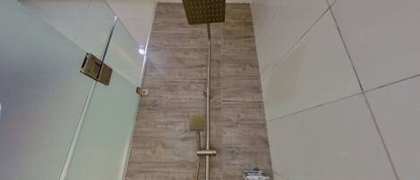 A modern bathroom with a glass partition, a wooden floor, and a shower with a square head.