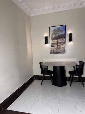 Un coin repas avec une table en marbre, des chaises noires et un tableau encadré accroché au mur.