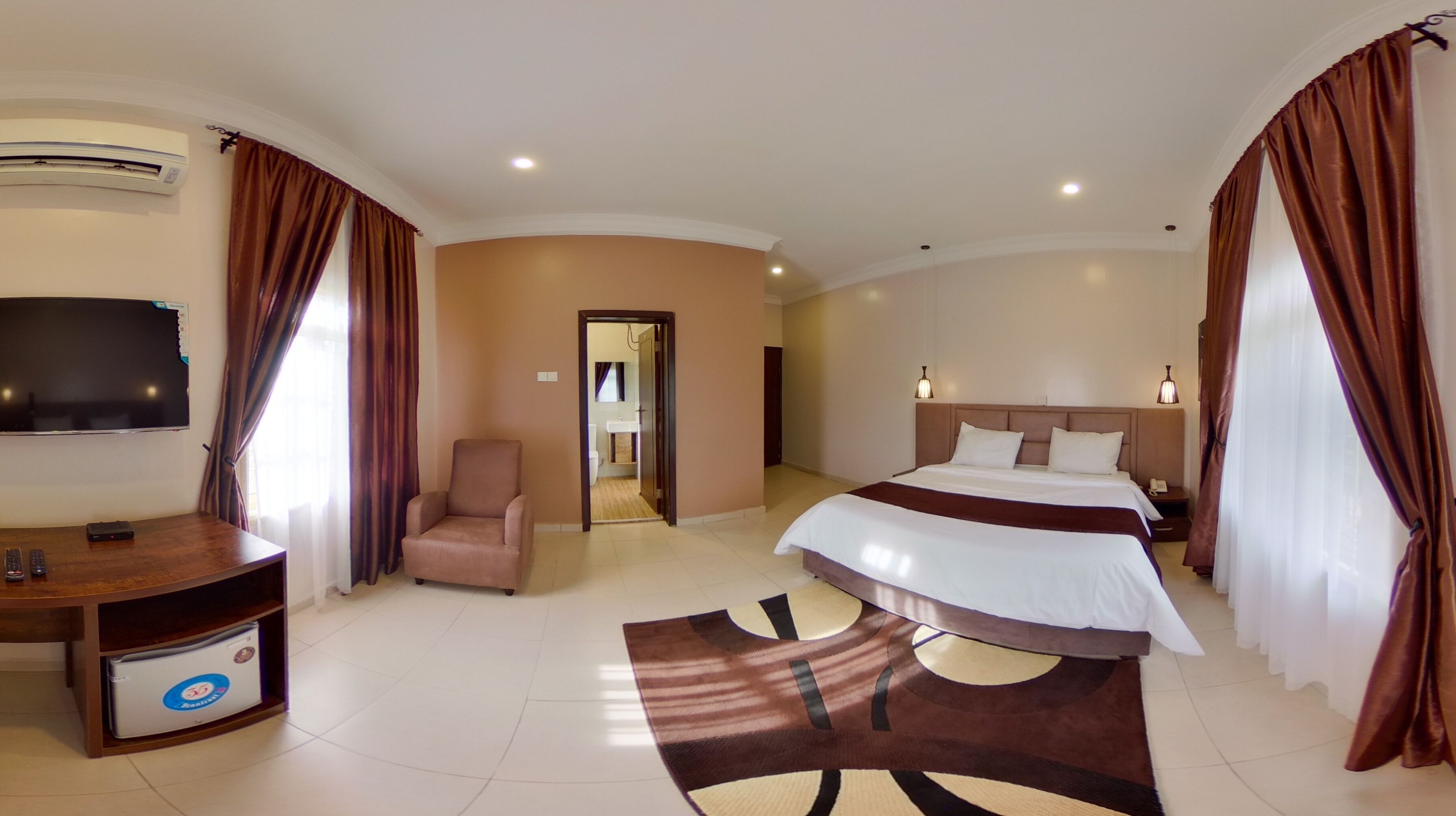 Ein Hotelzimmer mit Bett, Schreibtisch mit Stuhl, Fernseher und einem durchgegangenen Tür sichtbaren Badezimmer.