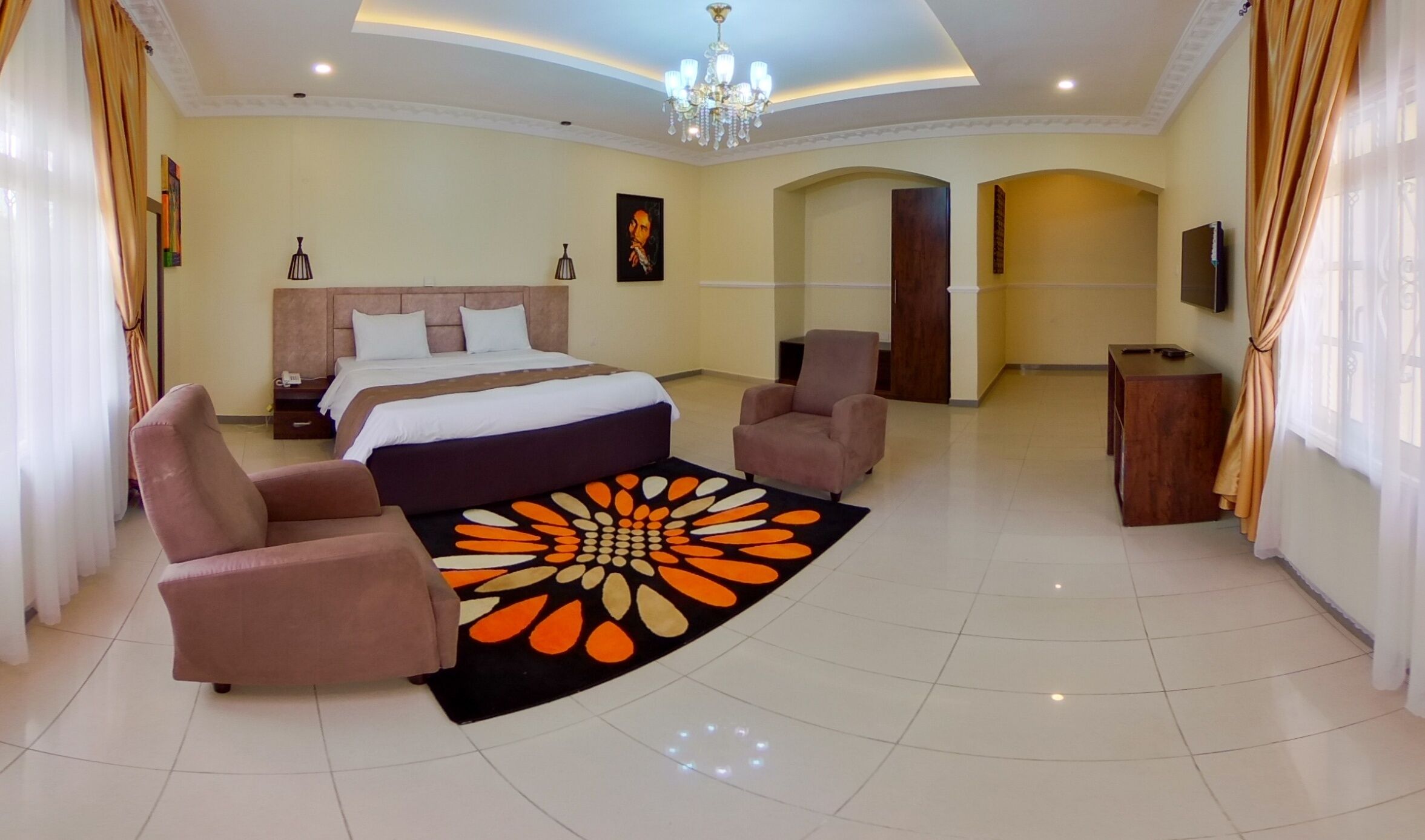 A spacious hotel room with a large bed, two armchairs, a desk, and a chandelier.