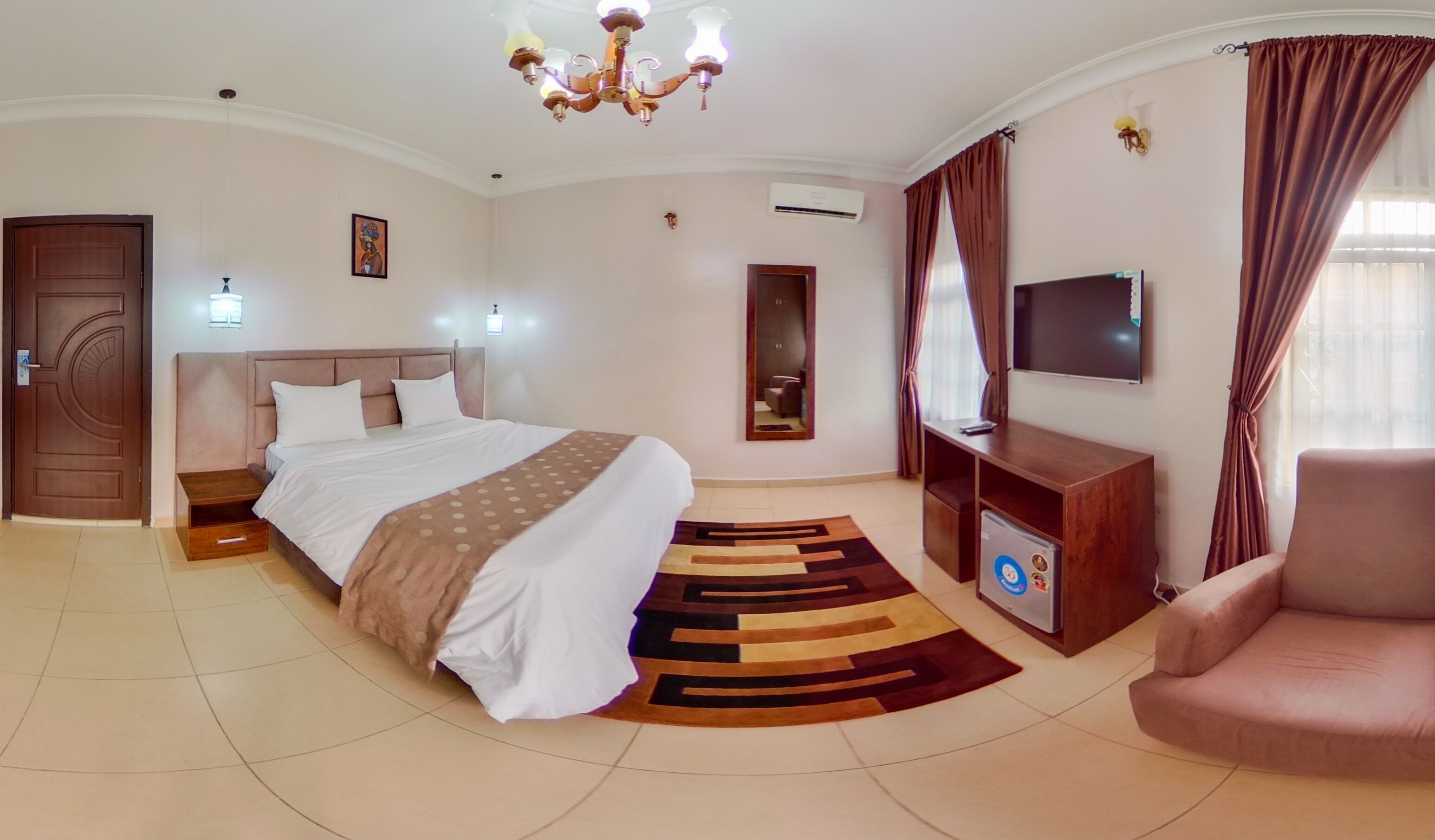 A hotel room with a large bed, a TV, a desk, a chair, and a chandelier.