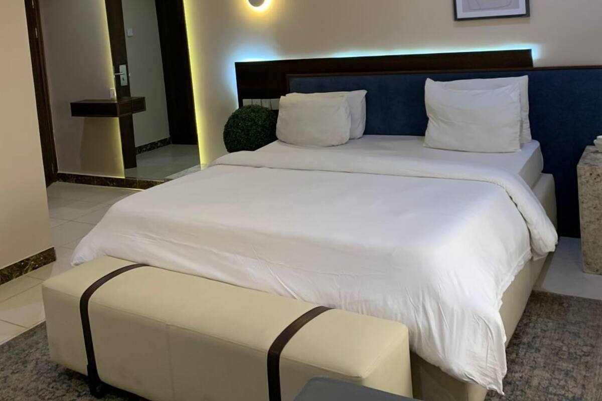 A modern hotel room with a large bed, a bedside table, a mirror, and a framed artwork on the wall.