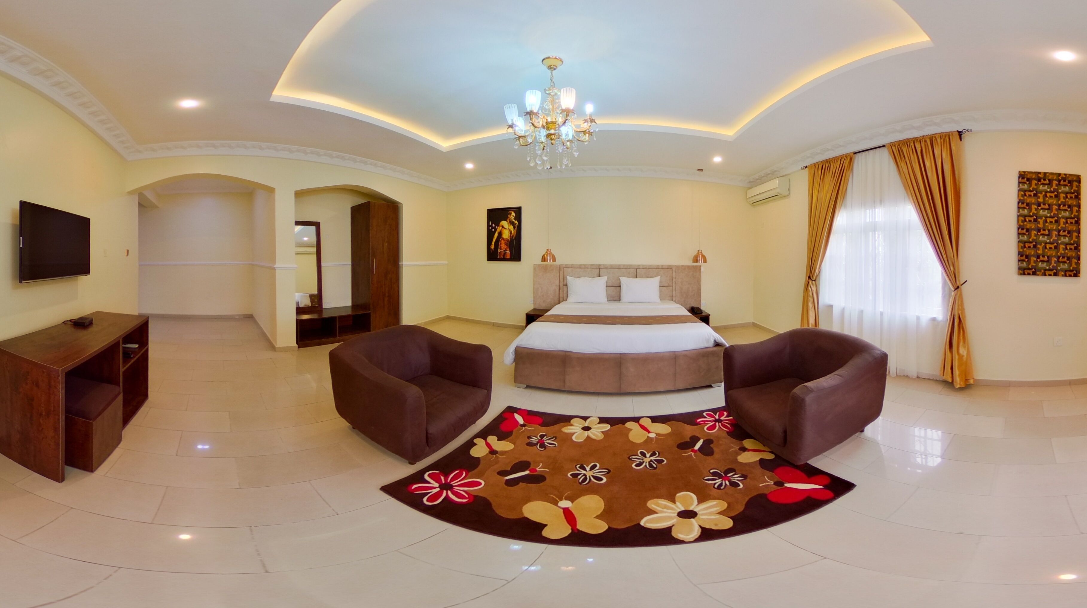 A spacious hotel room with a large bed, two armchairs, a TV, and a decorative rug.