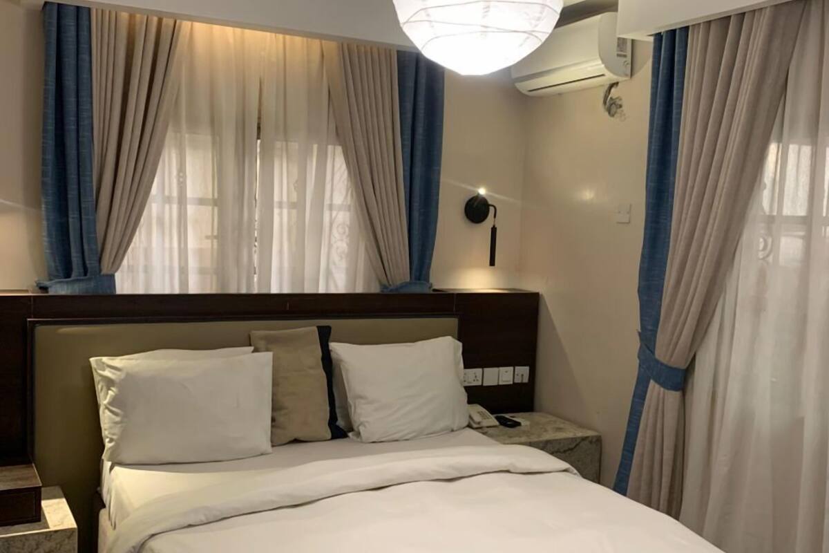 A hotel room with a bed, a nightstand, a lamp, and a ceiling light.