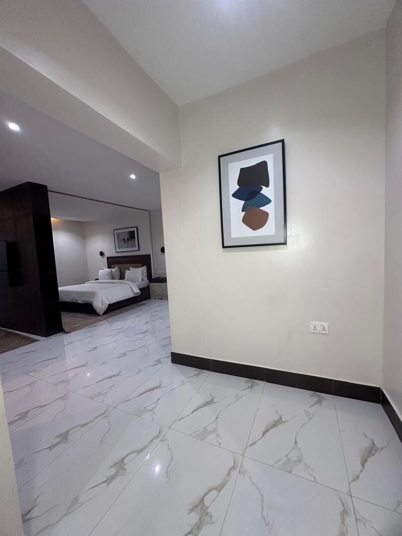A modern hotel room with a marble floor, a bed, a nightstand, and a framed artwork on the wall.