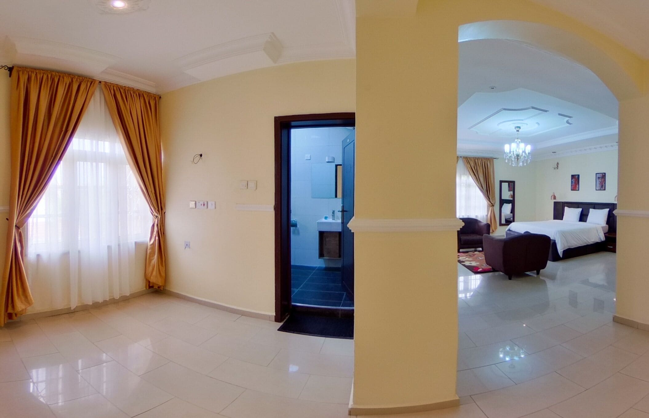 Une chambre d’hôtel avec un grand lit, un coin salon avec un canapé et une salle de bain visible à travers une porte ouverte.