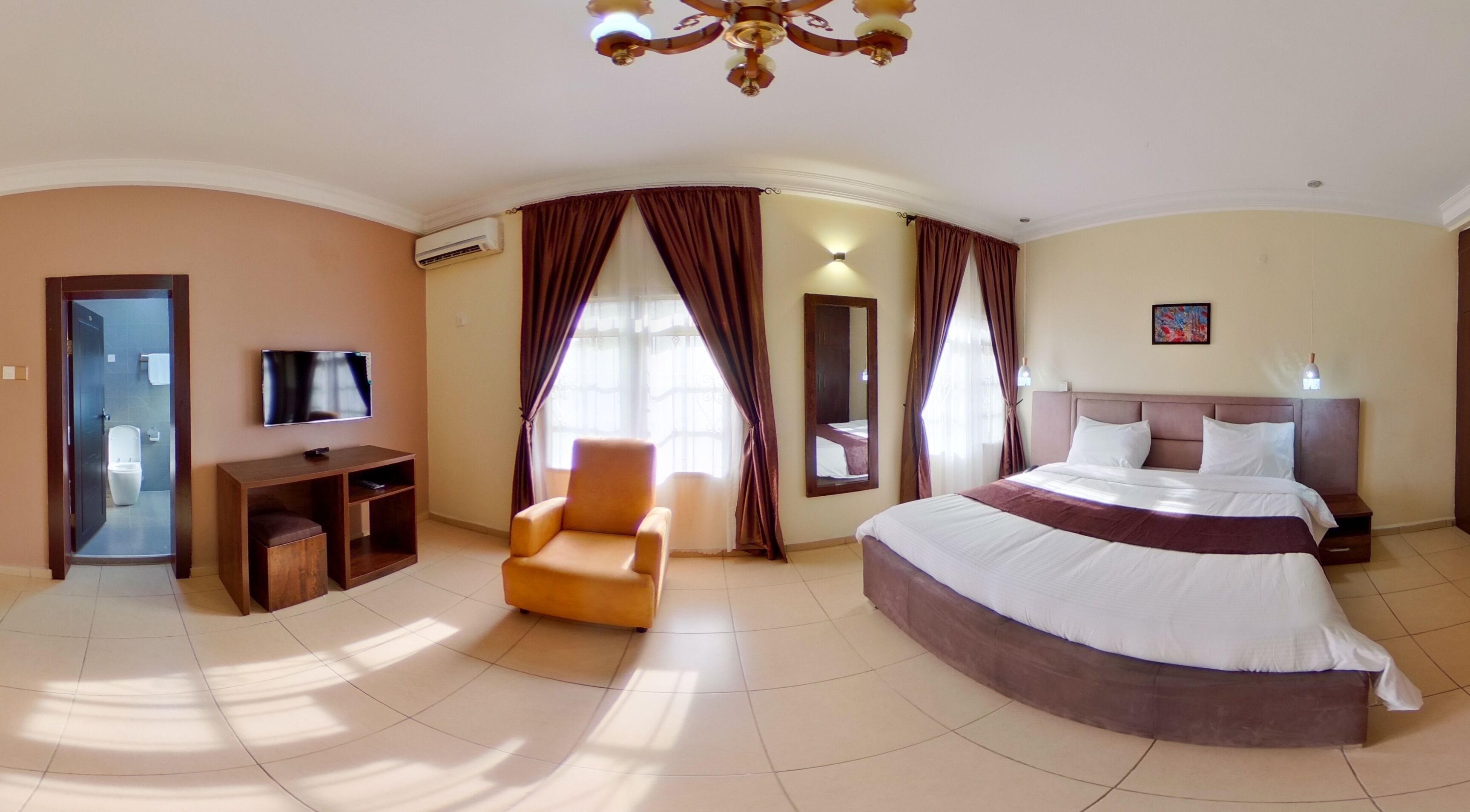 A hotel room with a bed, a TV, a chair, a desk, and an air conditioning unit.
