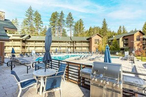 Un espace aménagé au bord de la piscine, avec des chaises longues, un barbecue et une vue sur un immeuble doté d’un balcon.
