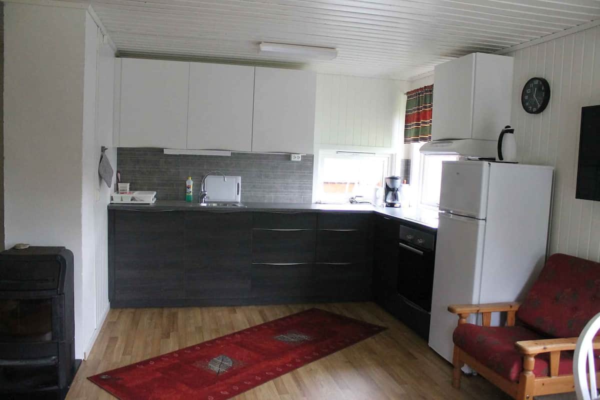 A compact kitchen with dark cabinets, a white refrigerator, and a red rug.