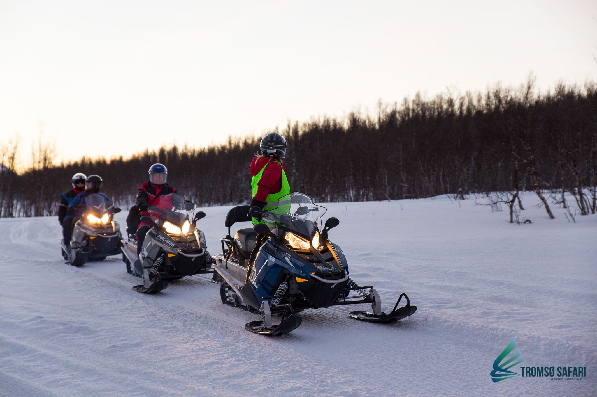 Three snowmobiles on a snowy path with a forest in the background.