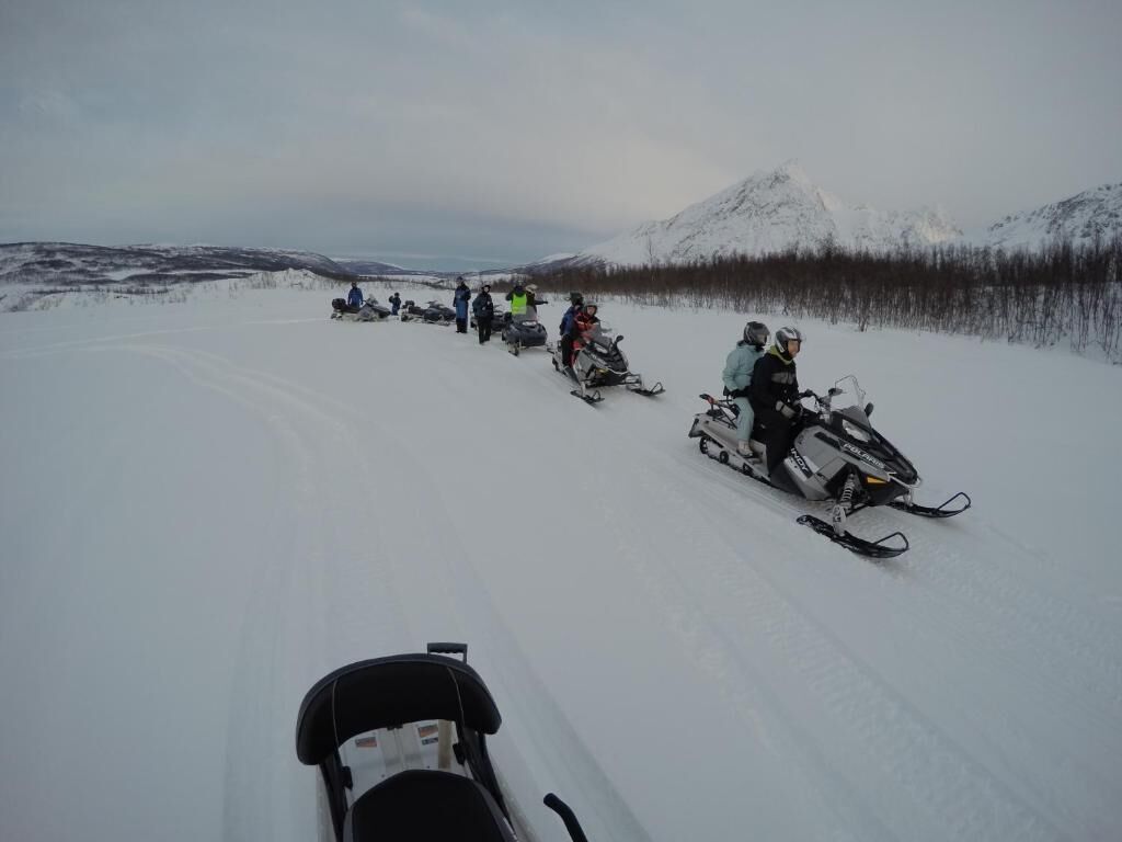 Un grupo de personas circulando en motos de nieve sobre un paisaje nevado.