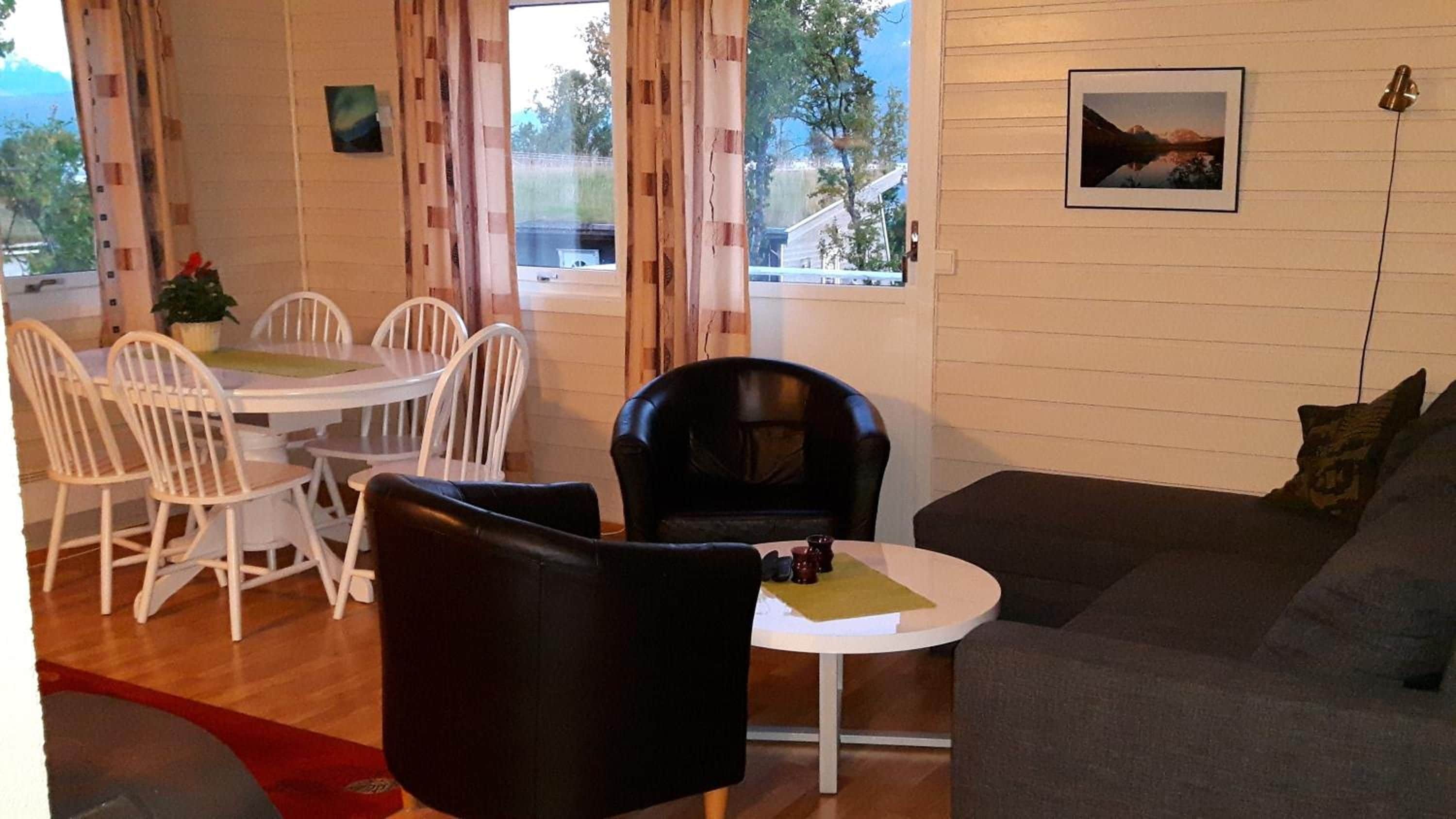 Een woonkamer met een bank, een eettafel met stoelen, een zwarte stoel en een raam met gordijnen.