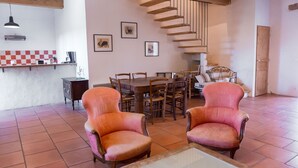 Une pièce spacieuse avec un escalier en bois, un coin repas comprenant une table et des chaises, ainsi que deux fauteuils.