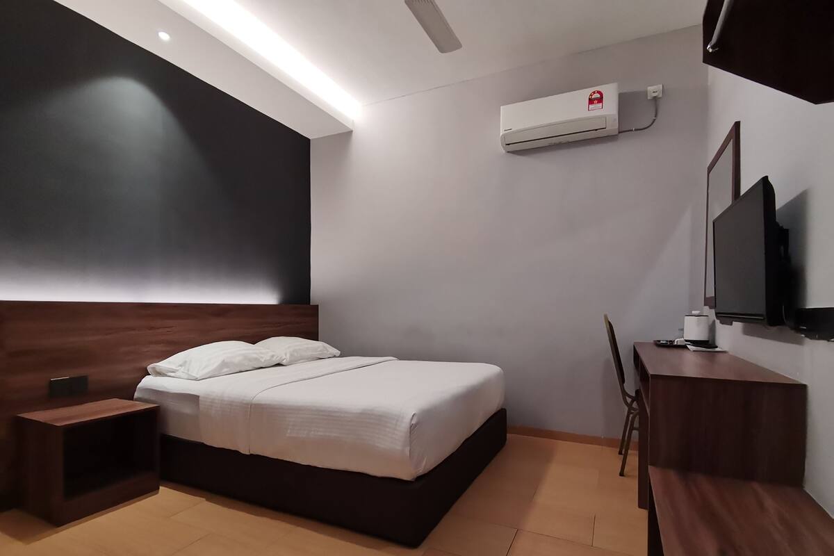 A modern hotel room with a bed, bedside table, desk, chair, TV, and air conditioning unit.