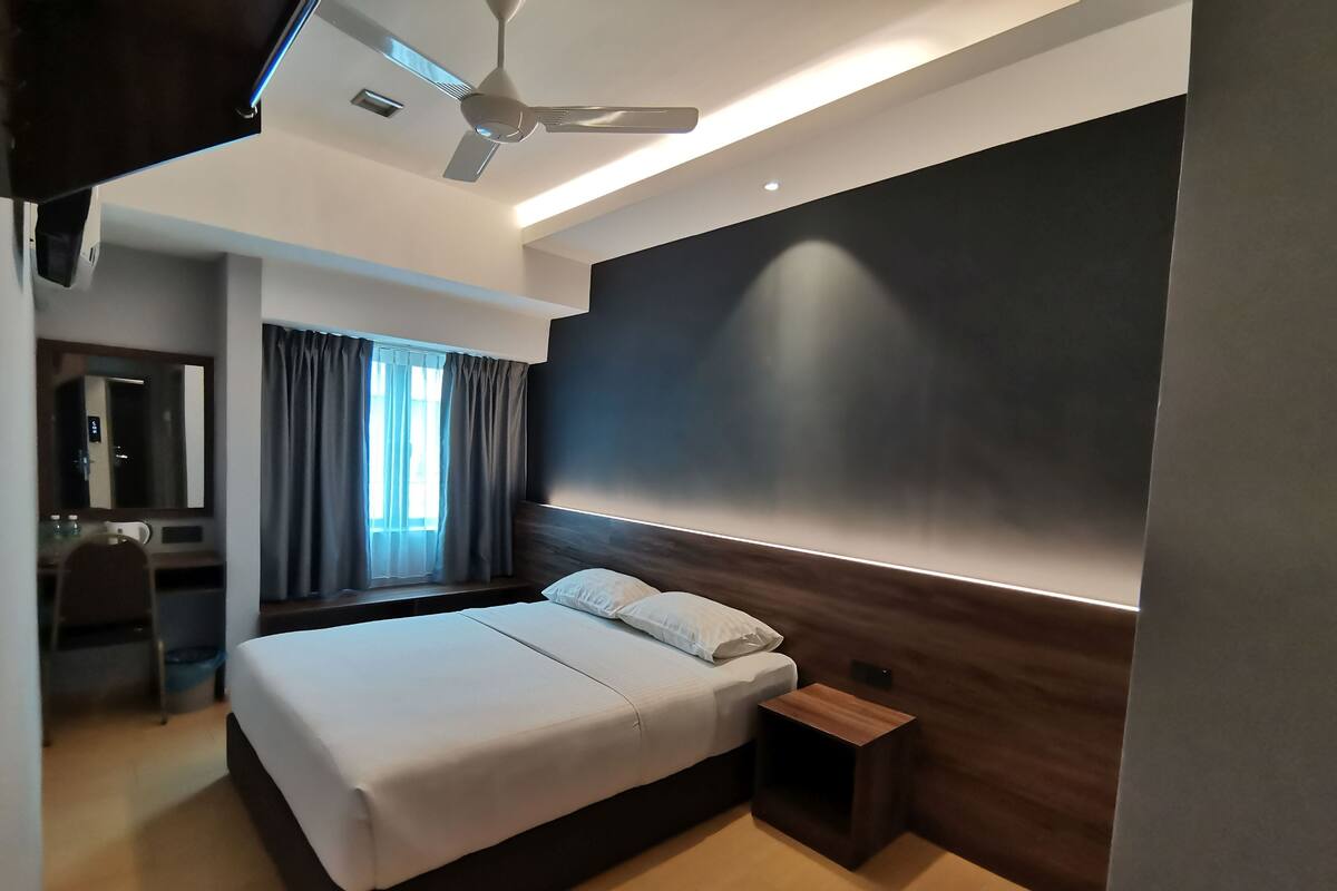 A modern hotel room with a large bed, a desk, and a ceiling fan.