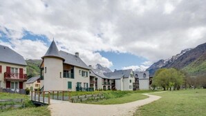 Una hilera de casas de estilo europeo tradicional con una torre central, un camino empedrado y montañas al fondo.