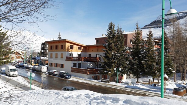 A snow-covered street with buildings, a lamppost, and a mountain in the background.