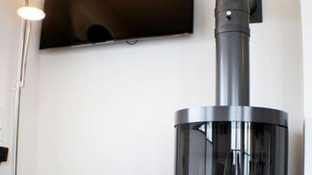 A modern living room with a grey sofa, a black wood-burning stove, and a mounted flat-screen TV. - Sielhuus 1 - Exclusive first floor apartment with sauna and box-spring beds (Fedderwardersiel-Butjadingen)
