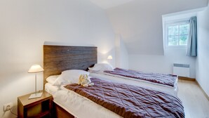 Ein Hotelzimmer mit zwei Betten, einem Holzkopfteil, Nachttischlampen und einem Fenster mit Vorhängen.
