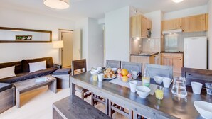 Ein modernes Wohnzimmer mit einer Couch, einem Couchtisch und einem Essbereich, gedeckt für ein Frühstück.