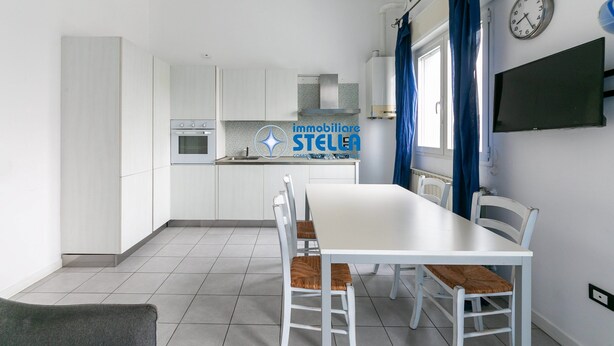 A modern kitchen with white cabinets, a dining table with chairs, a clock, and a TV on the wall. - Milan's Apartment n.1 (Jesolo)