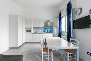 Una cocina moderna con armarios blancos, una mesa de comedor con sillas, un reloj y un televisor en la pared.