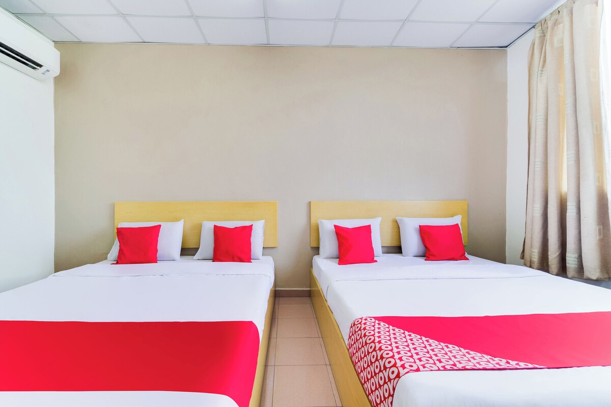 A hotel room with two beds, each with white bedding and red pillows.