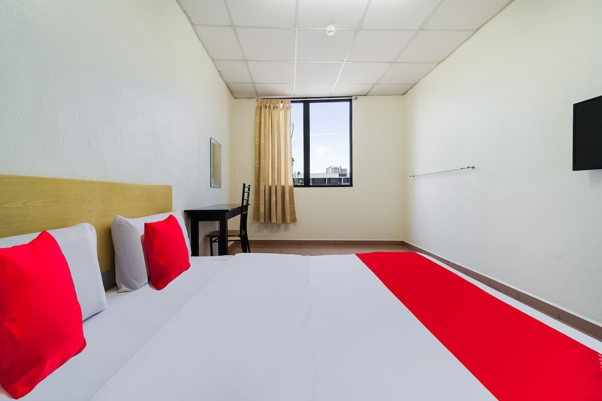 A hotel room with a bed, a desk, a chair, a window with curtains, and a flat-screen TV mounted on the wall.
