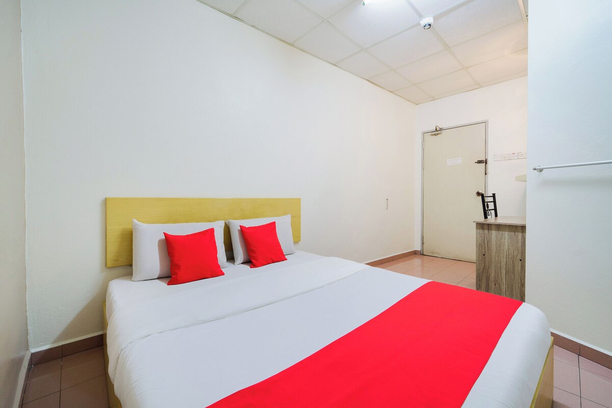 A hotel room with a bed, a wooden headboard, a white and red bedspread, and a door in the background.