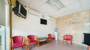 A hotel lobby with a reception desk, four wooden chairs with pink cushions, a clock, and air conditioning units on the wall. - OYO 89461 CP Hotel (Butterworth)