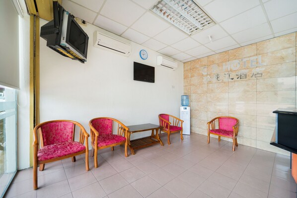 A hotel lobby with a reception desk, four wooden chairs with pink cushions, a clock, and air conditioning units on the wall. - OYO 89461 CP Hotel (Butterworth)