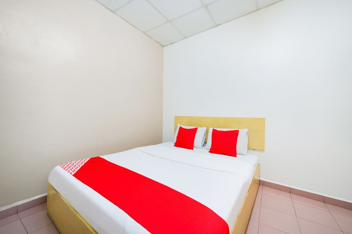 A neatly made bed with a white and red bedspread, a wooden headboard, and two red pillows.