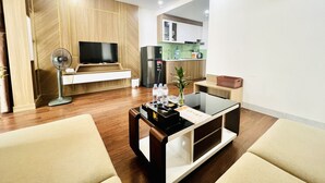 Ein modernes Wohnzimmer mit Flachbildfernseher, Standventilator und Couchtisch mit einer Zeitschrift.